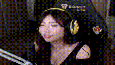 a woman wearing headphones is sitting in a gaming chair in front of a microphone and sticking her tongue out .