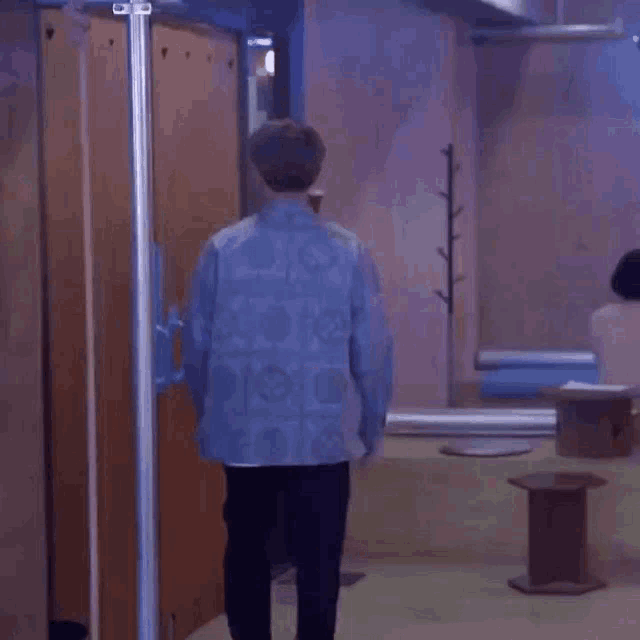 a man in a blue shirt and black pants is standing in a room with a pole .