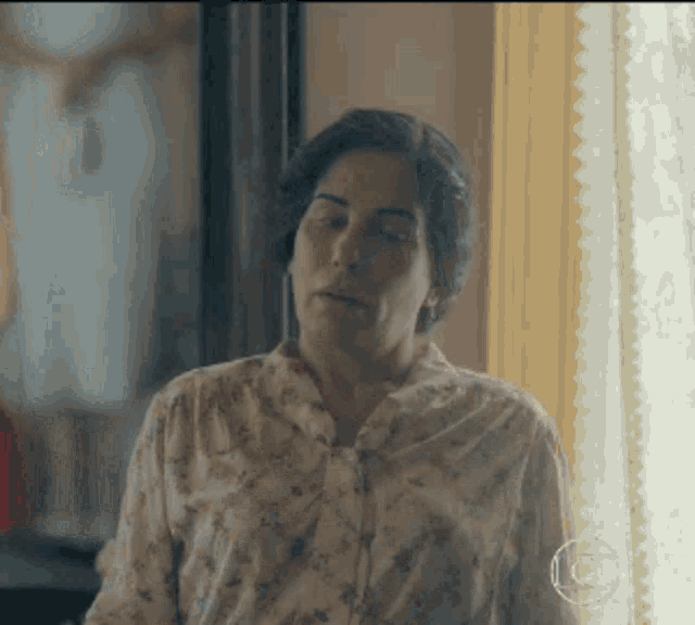 a woman in a floral shirt is standing in front of a window looking out .