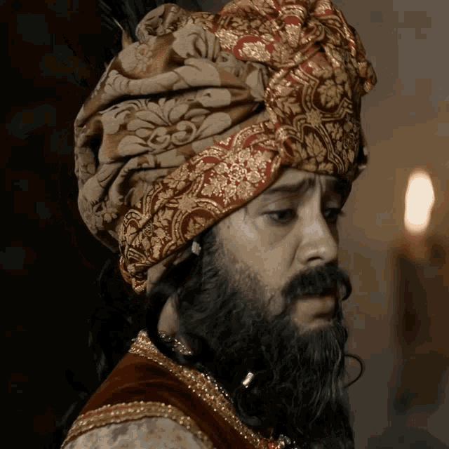 a man with a beard wearing a turban with a feather on it