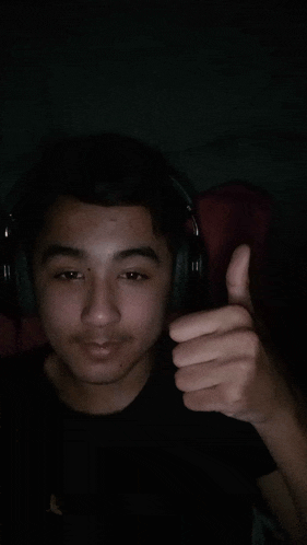 a young man wearing headphones gives a thumbs up sign