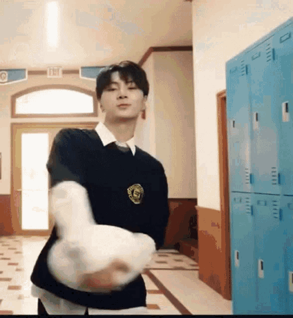 a young man in a school uniform is standing in a hallway holding a white item .