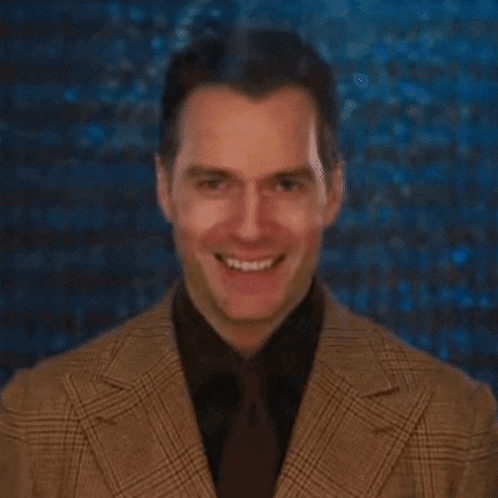 a man in a suit and tie is smiling in front of a blue wall .