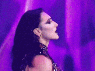 a woman is standing in front of a purple background with her eyes closed and her hair blowing in the wind .