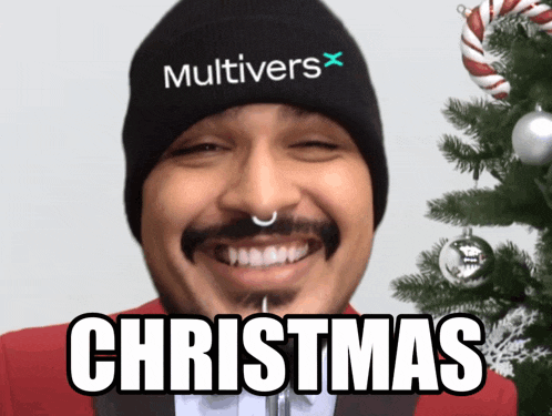 a man wearing a beanie that says " multivers " is smiling in front of a christmas tree