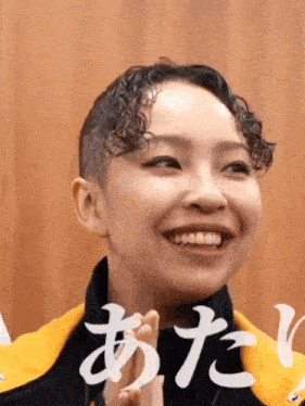 a woman with curly hair and a shaved head is smiling and making a funny face .