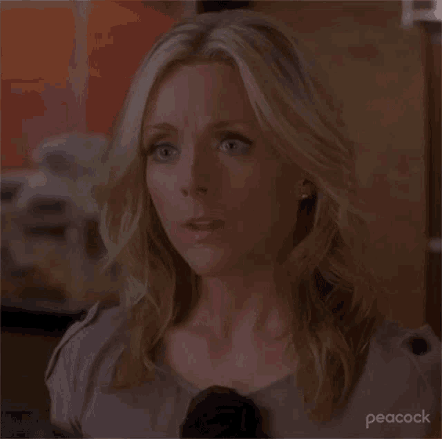 a woman with blonde hair and blue eyes is making a surprised face .