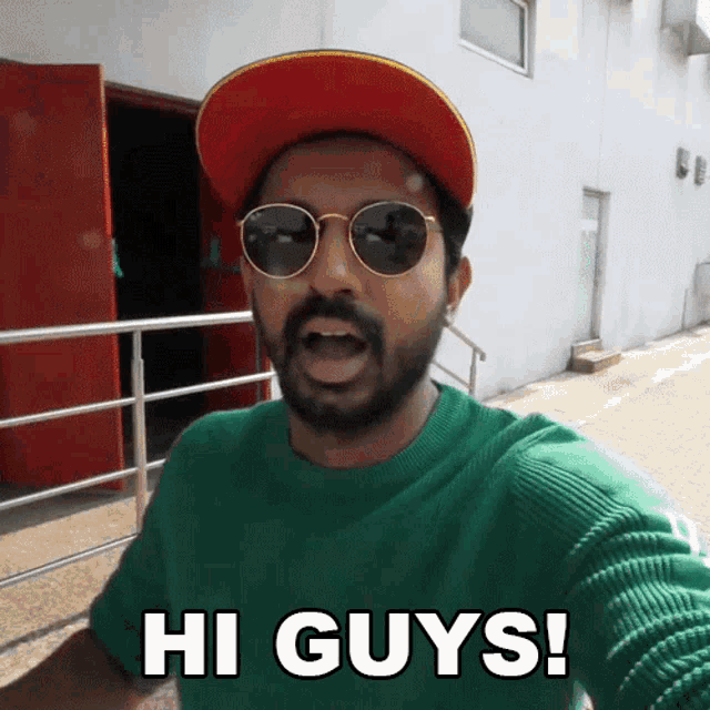 a man wearing sunglasses and a hat says hi guys in front of a building