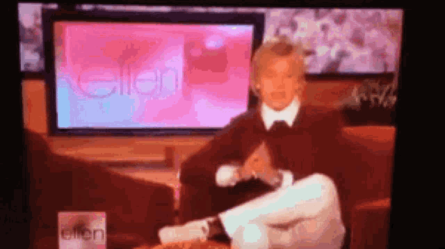 a woman is sitting on a couch in front of a television screen that says ellen .