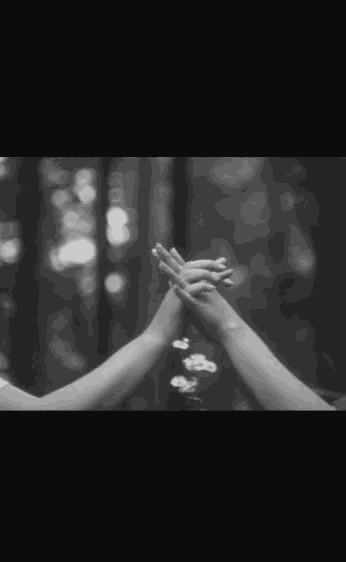a black and white photo of two people holding hands in a forest
