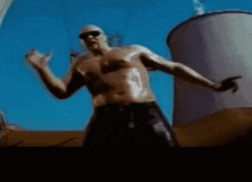 a man without a shirt is dancing in front of a large white tank