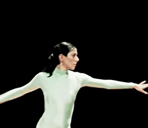 a woman in a white bodysuit is standing with her hands behind her head