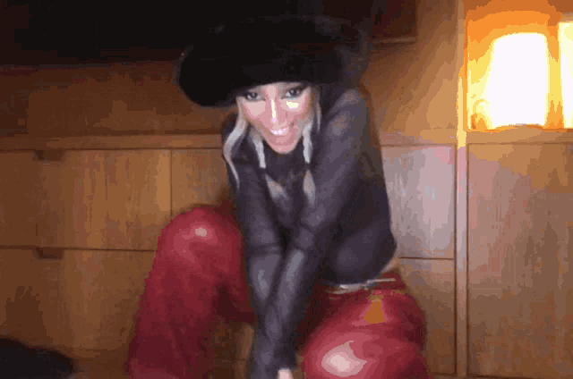 a woman in a black hat and red pants is smiling