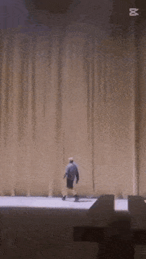 a man is walking on a stage in front of a curtain with the letter m on it