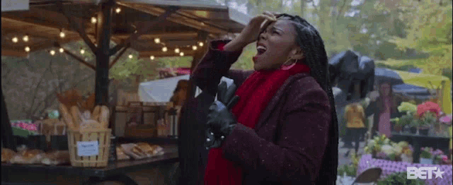 a woman in a red scarf is standing in front of a bakery and holding her head .
