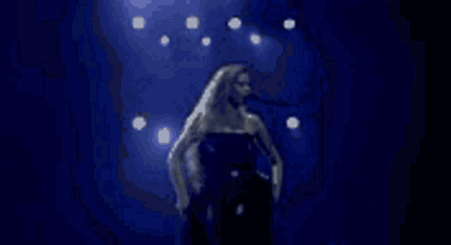 a woman is singing into a microphone on a stage in front of a crowd of people .