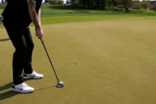 a man with a tattoo on his arm is putting on a golf course