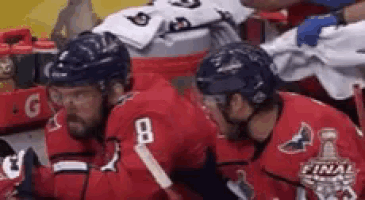 two hockey players are sitting in a locker room talking to each other .
