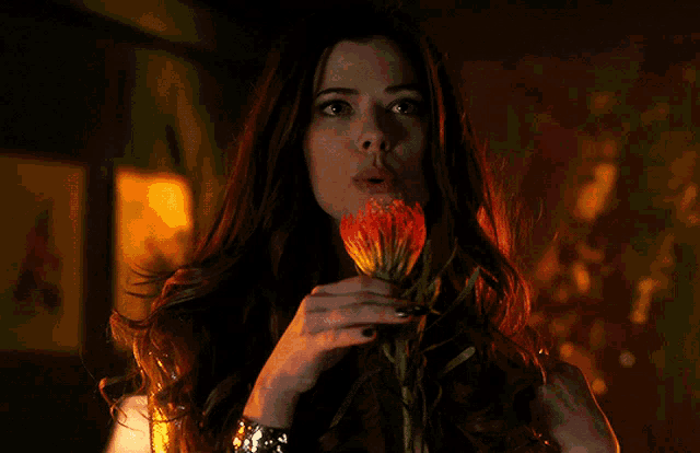 a woman is holding a flower in her hand and smelling it