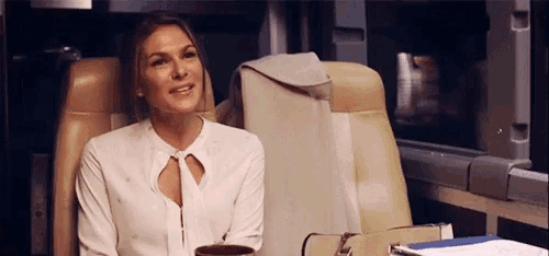 a woman in a white shirt is sitting in a chair with a cup of coffee in her hand .