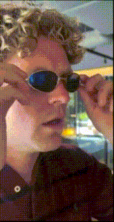 a man with curly hair wearing sunglasses and a maroon shirt