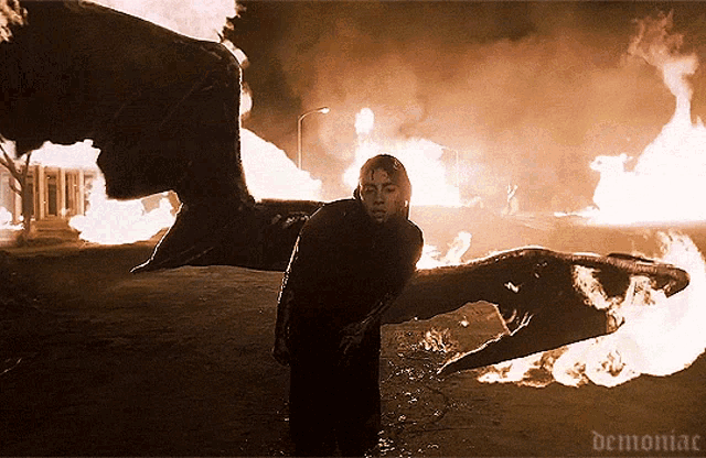 a demon with wings is standing in front of a fire with demoniac written on the bottom