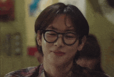 a man wearing glasses and a plaid shirt smiles for the camera