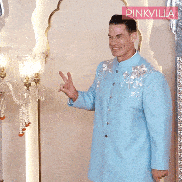 a man in a light blue suit stands in front of a pinkvilla banner