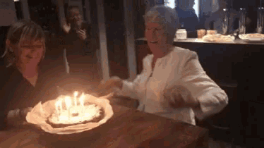 two women are sitting at a table with a birthday cake with candles