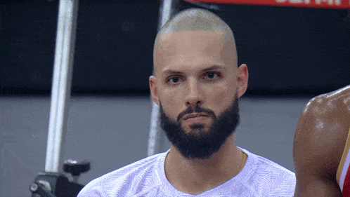 a man with a beard wearing a purple shirt looks at the camera