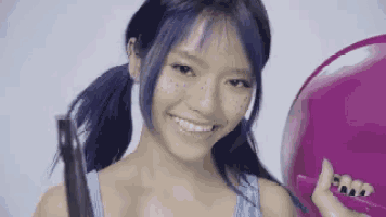 a woman with blue hair and freckles is smiling while holding a purple balloon .