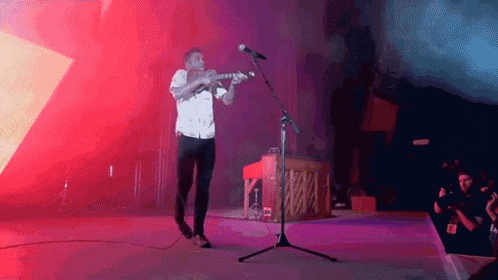 a man is playing a violin and singing into a microphone on stage .