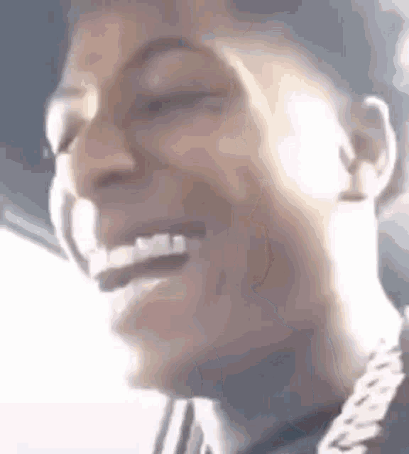 a close up of a man 's face laughing with his eyes closed and a chain around his neck .
