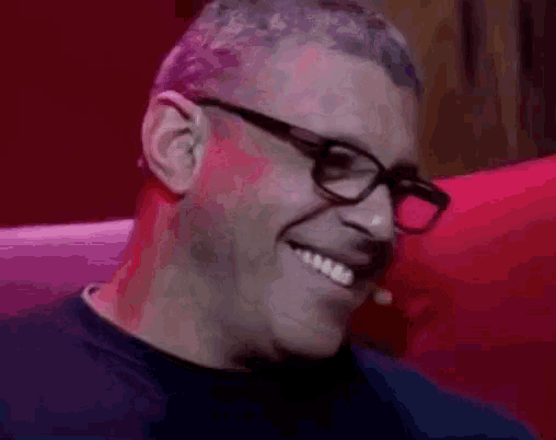 a man wearing glasses is smiling while sitting in a red chair .