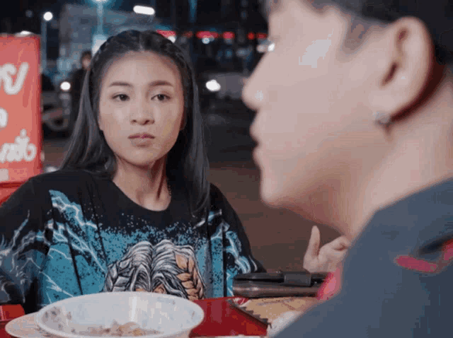 a man and a woman are sitting at a table and the woman is wearing a shirt with a lightning bolt on it