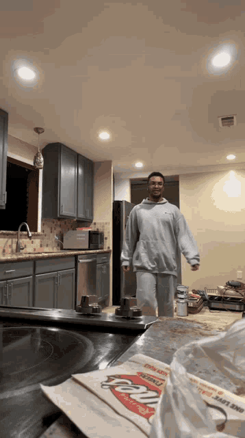 a man standing in a kitchen with a bag of pizza