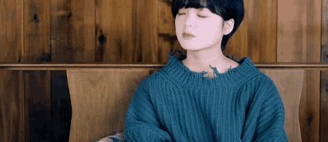 a woman wearing a blue sweater with a tattoo on her shoulder sits with her eyes closed