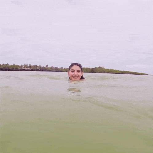a woman in a bikini is swimming in a body of water with her mouth open