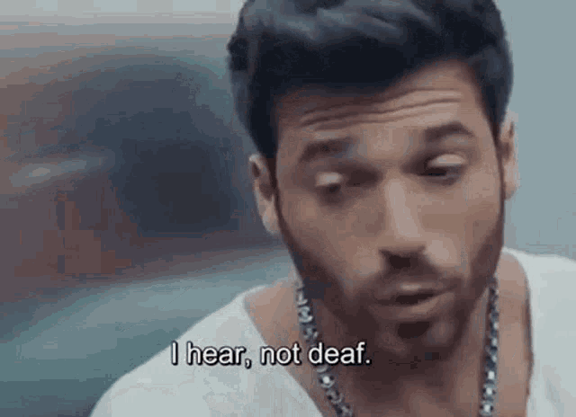 a man with a beard is wearing a white shirt and a chain around his neck .
