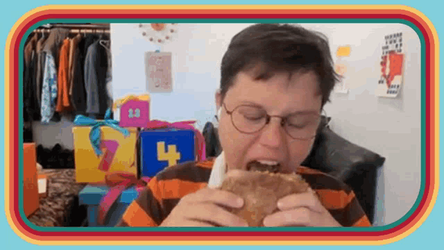 a man wearing glasses is eating a hamburger in a room with gifts .
