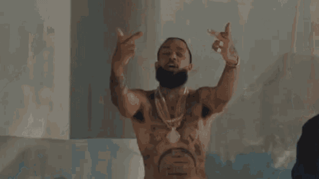 a shirtless man with tattoos on his chest is dancing in a room with a man standing behind him .