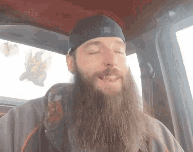 a man with a long beard is sitting in a car with his eyes closed and smiling .