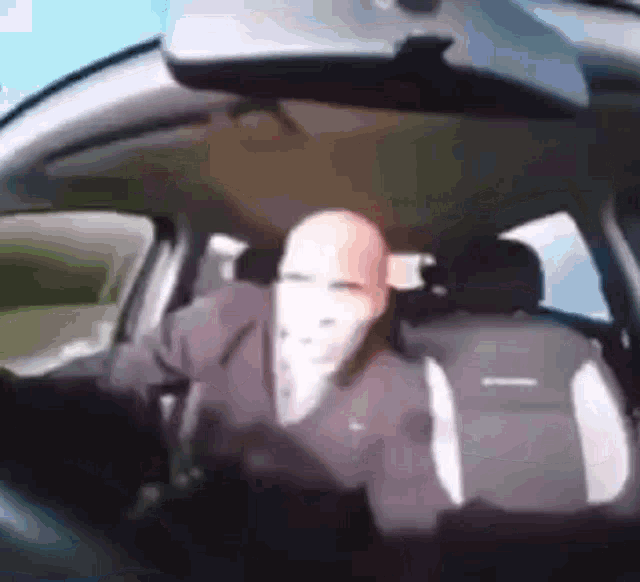 a man in a suit and tie is driving a car with a mask on his face .