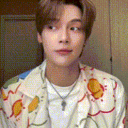 a young man wearing a white shirt and a necklace is looking at the camera .