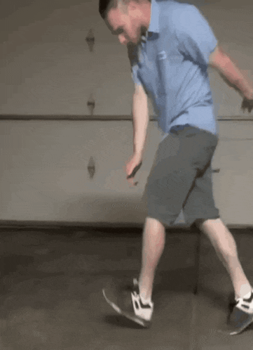 a man in a blue shirt and grey shorts is riding a skateboard