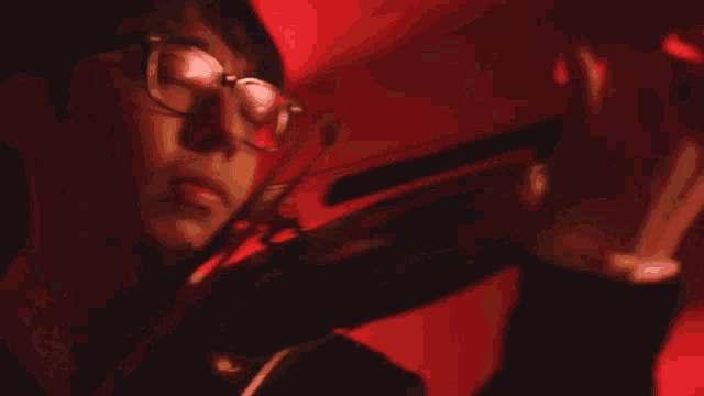 a man with glasses is playing a violin in a red light
