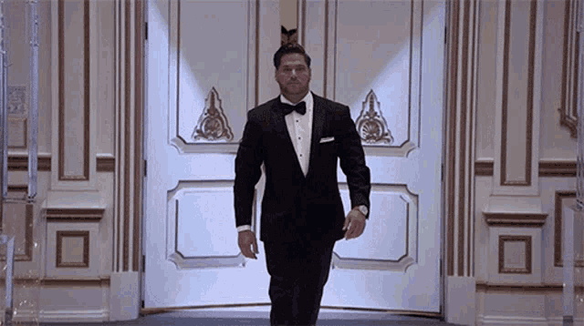 a man in a tuxedo and bow tie is walking into a doorway
