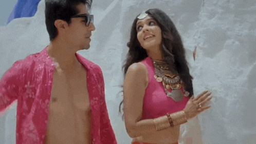 a man and a woman are standing next to each other on a beach . the woman is wearing a pink top .