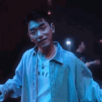 a young man in a blue jacket is standing in a dark room with his arms outstretched .