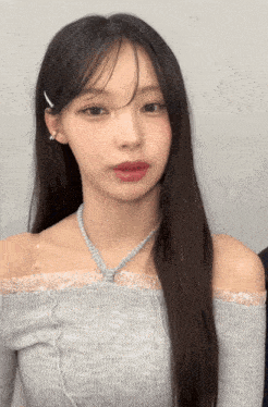 a woman with long hair is wearing a grey off the shoulder top and a necklace